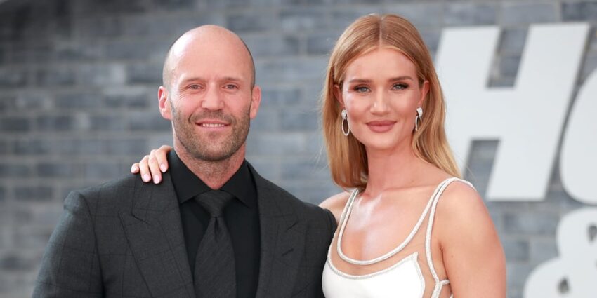 Jason Statham and Rosie Huntington Whiteley smiling, looking slightly to the right with a logo that has the letter H peeking behind them
